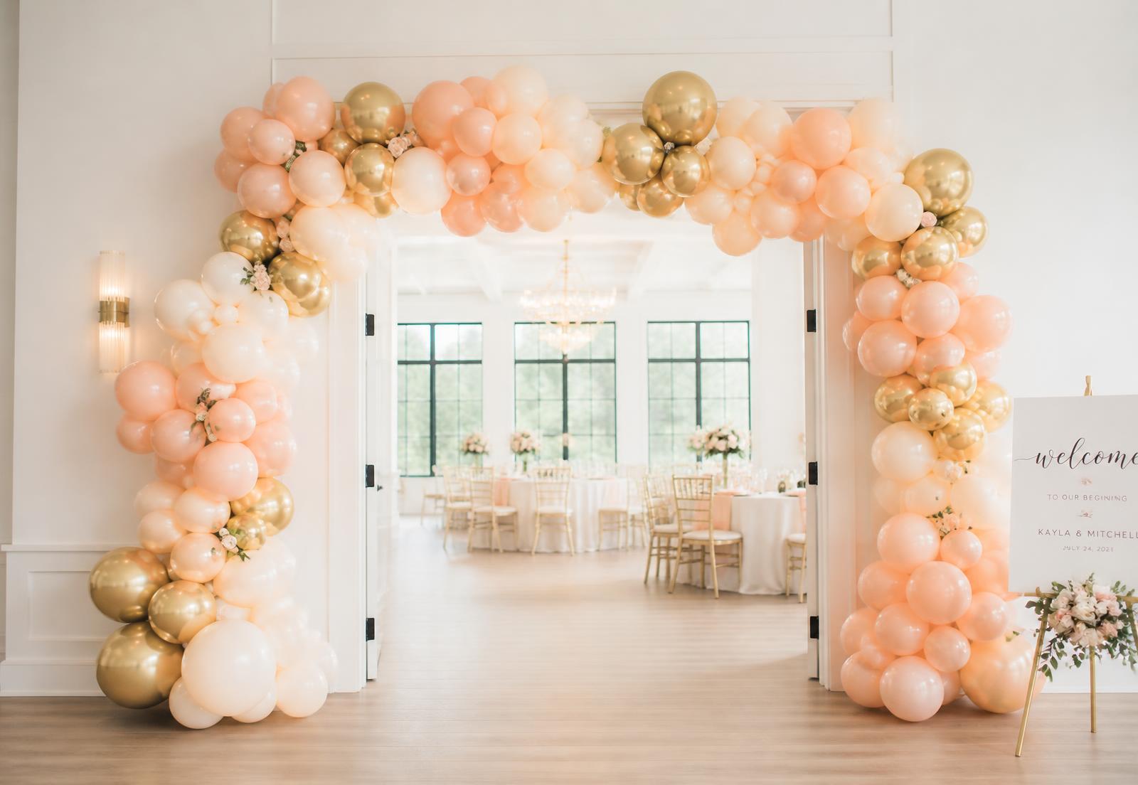 Peach and gold balloon arch framing the entrance of a bright event venue